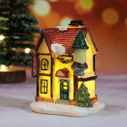 Decorative miniature house with lights on a snowy base, Christmas tree in the background